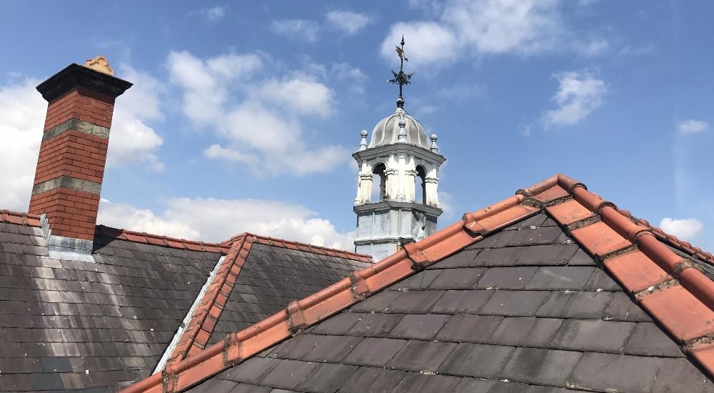 Slate roof, chimney and lead-clad turret with weather vane.